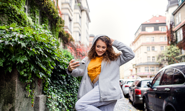 Portrait of young woman with smartphone outdoors on street, video for social media concept.