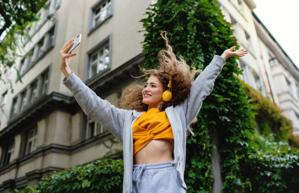 Portrait of young woman with smartphone dancing outdoors on street, video for social media concept.