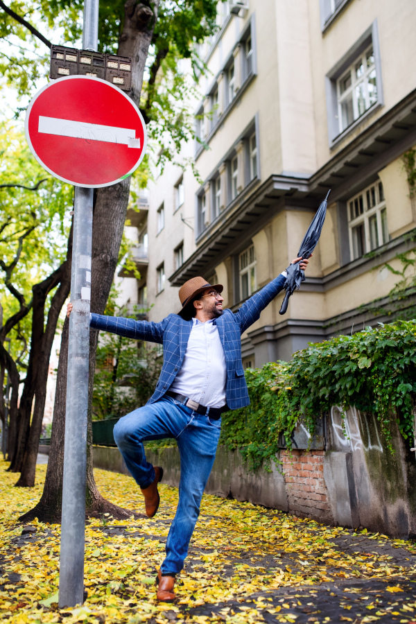 Portrait of young man with umbrella holding onto lamp post outdoors on street, social media concept.