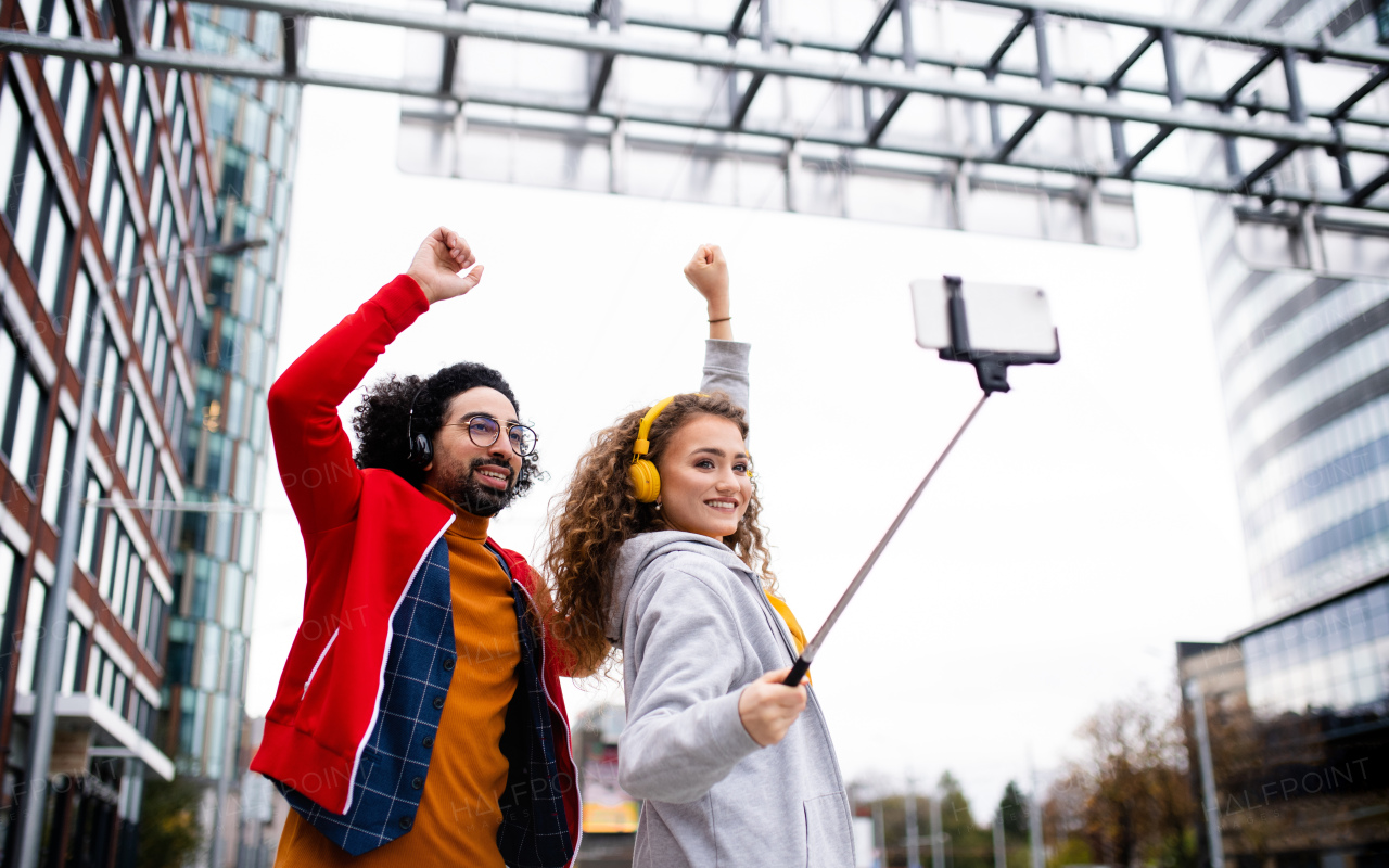 Portrait of young couple with smartphone making video for social media outdoors on street.