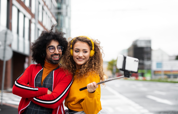 Portrait of young couple with smartphone making video for social media outdoors on street.