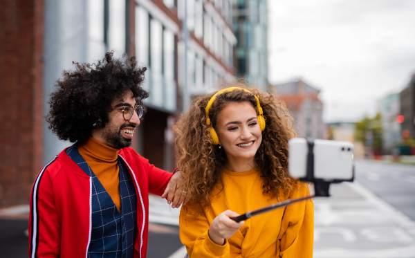 Portrait of young couple with smartphone making video for social media outdoors on street.