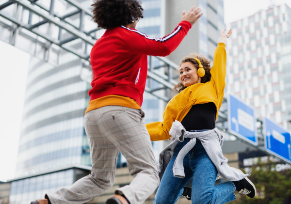 Portrait of young couple with smartphone making video for social media outdoors on street, jumping.