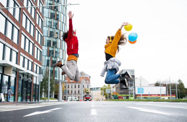 Side view of young couple with balloons jumping outdoors on street, video for social media concept.