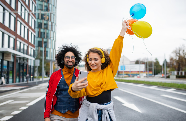 Portrait of young couple with smartphone making video for social media outdoors on street.