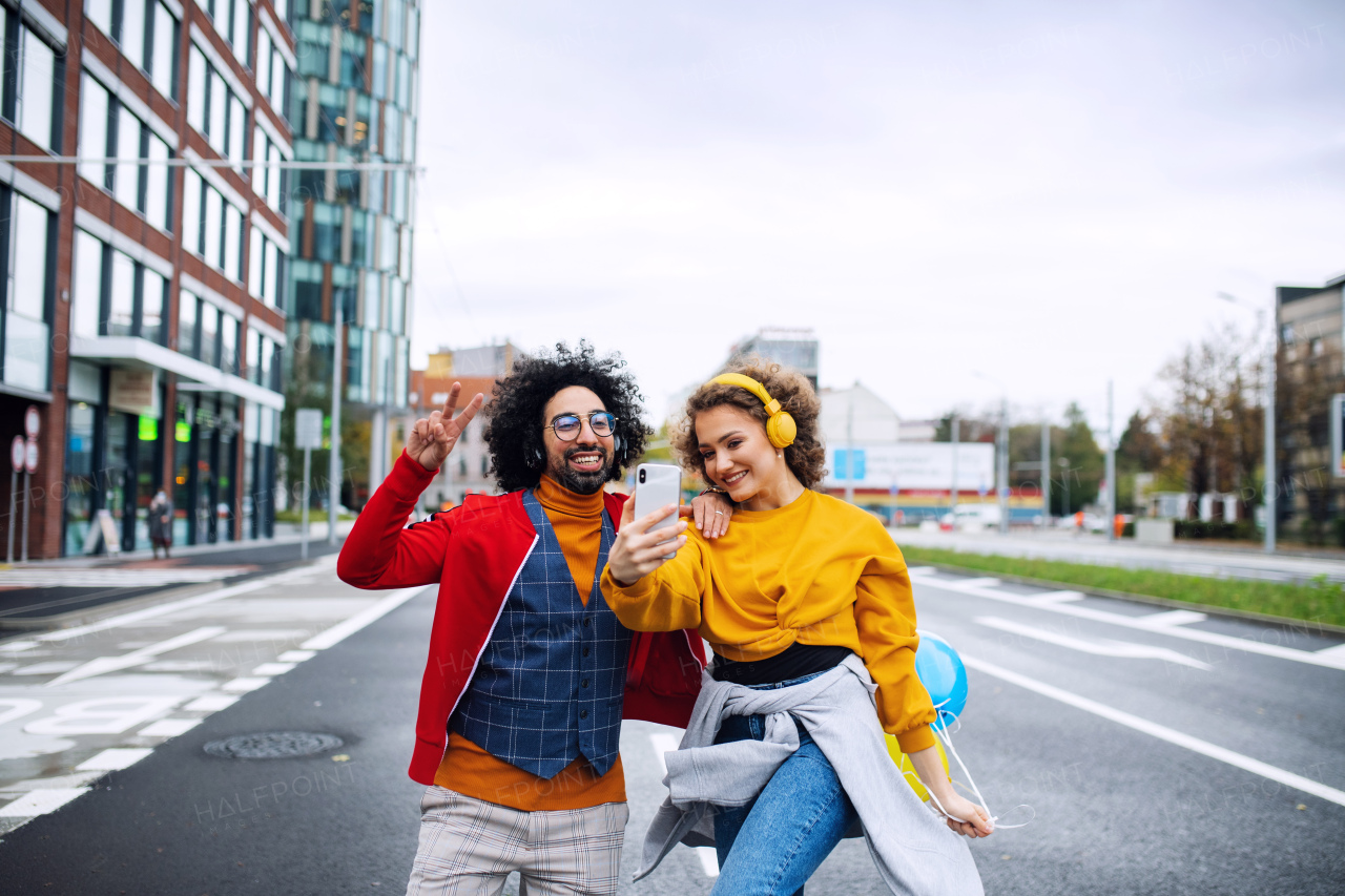 Portrait of young couple with smartphone making video for social media outdoors on street.