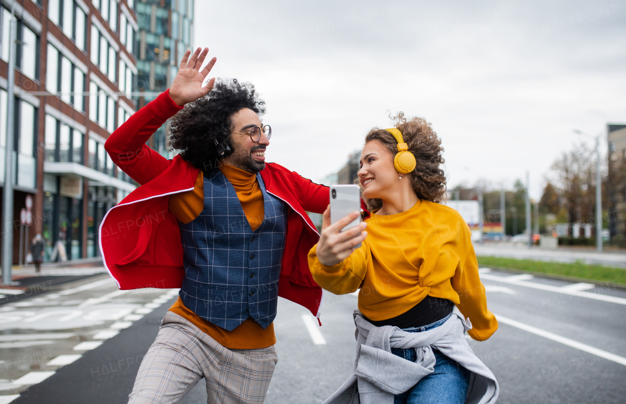 Portrait of young couple with smartphone making video for social media outdoors on street.