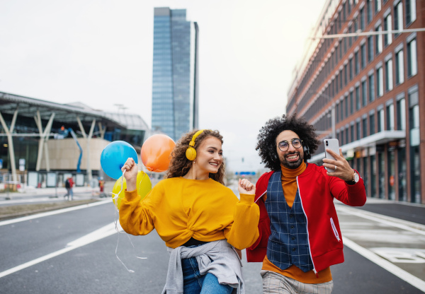 Portrait of young couple with smartphone making video for social media outdoors on street.