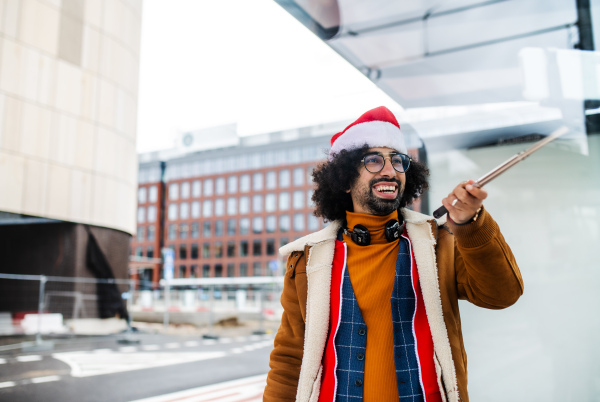 Young man with Santa hat making video for social media outdoors on bus stop. Copy space.