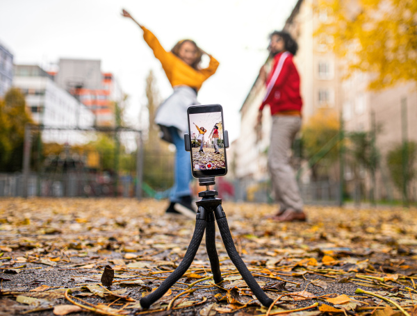 Portrait of young couple with smartphone making video for social media outdoors in park.