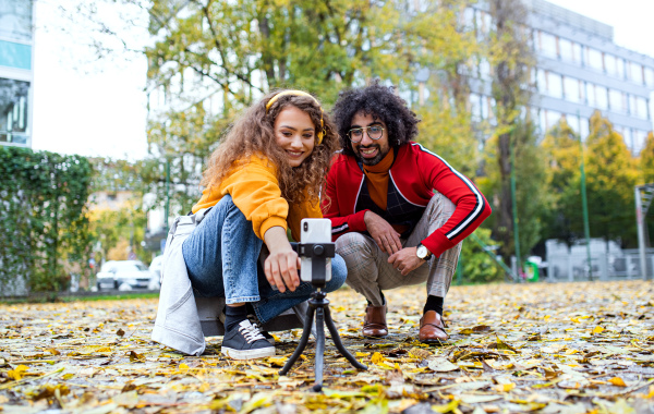 Portrait of young couple with smartphone making video for social media outdoors in park.