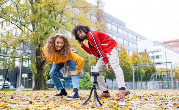 Portrait of young couple with smartphone making video for social media outdoors in park.