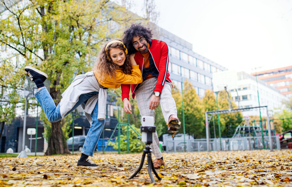 Portrait of young couple with smartphone making video for social media outdoors in park.