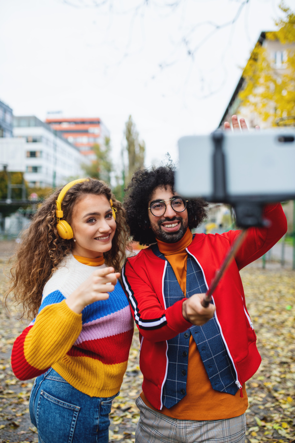 Portrait of young couple with smartphone making video for social media outdoors in city park.