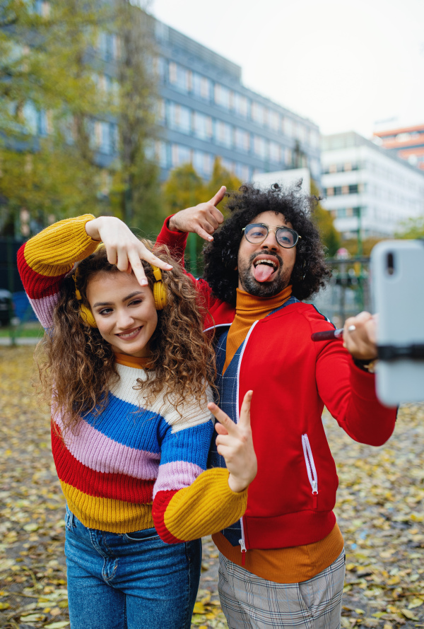 Portrait of young couple with smartphone making video for social media outdoors on street.