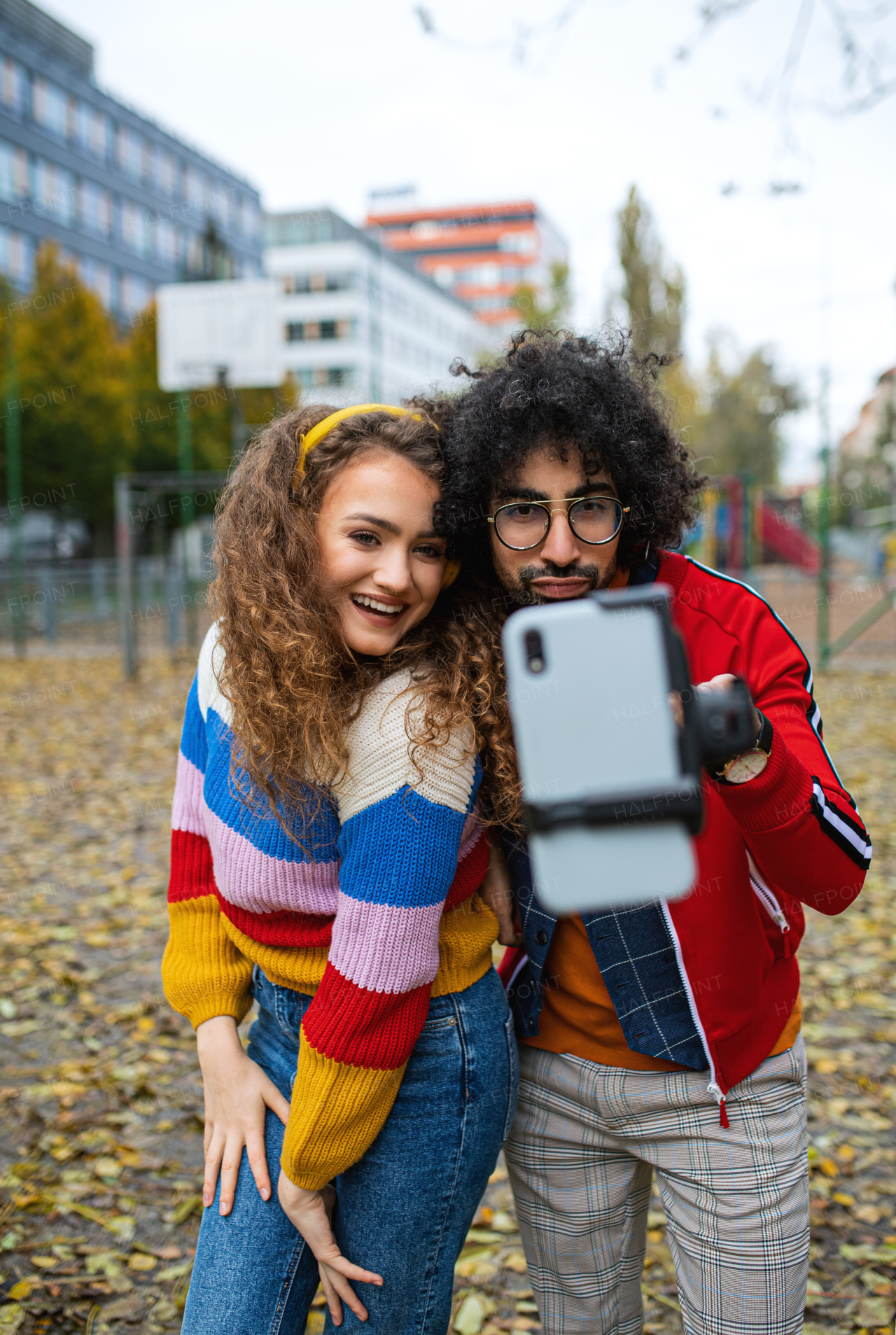 Portrait of young couple with smartphone making video for social media outdoors in park.