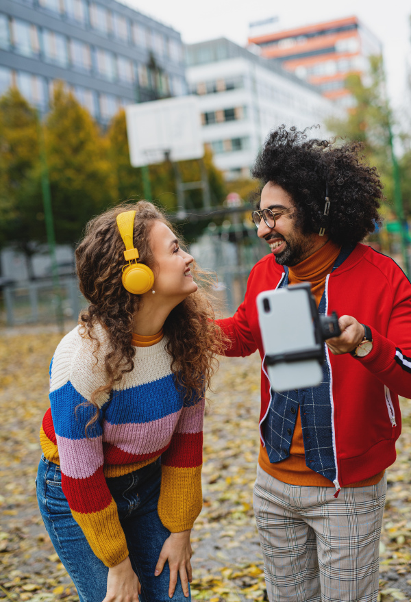 Portrait of young couple with smartphone making video for social media outdoors in park.