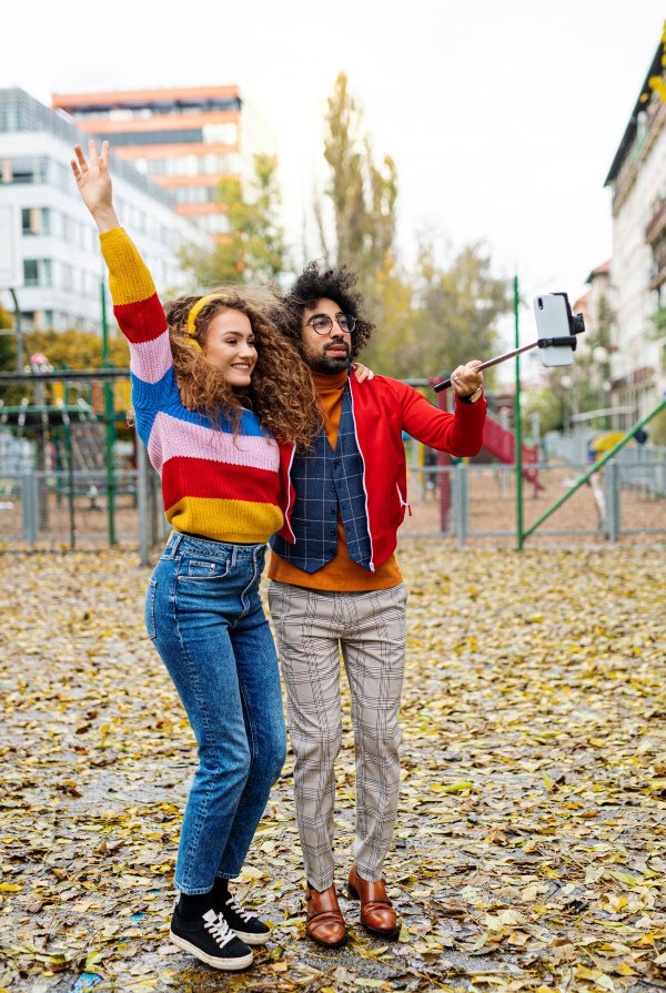 Portrait of young couple with smartphone making video for social media outdoors in park.