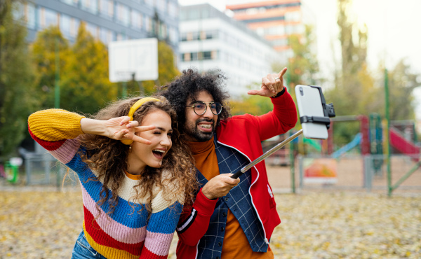 Portrait of young couple with smartphone making video for social media outdoors in park.