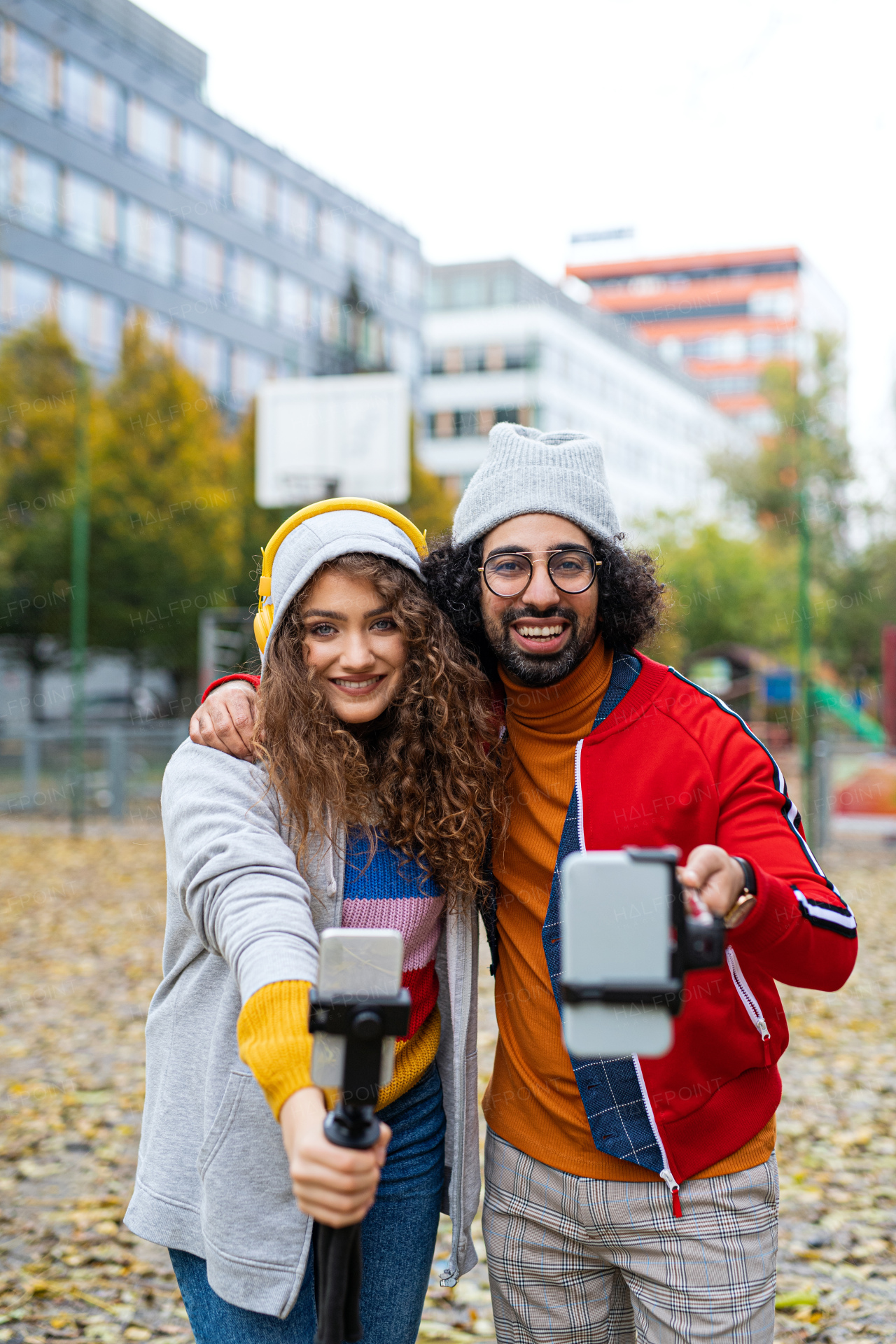 Portrait of young couple with smartphone making video for social media outdoors in park.