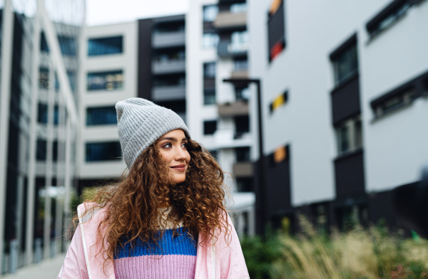 Portrait of young woman with hat standing outdoors on street.