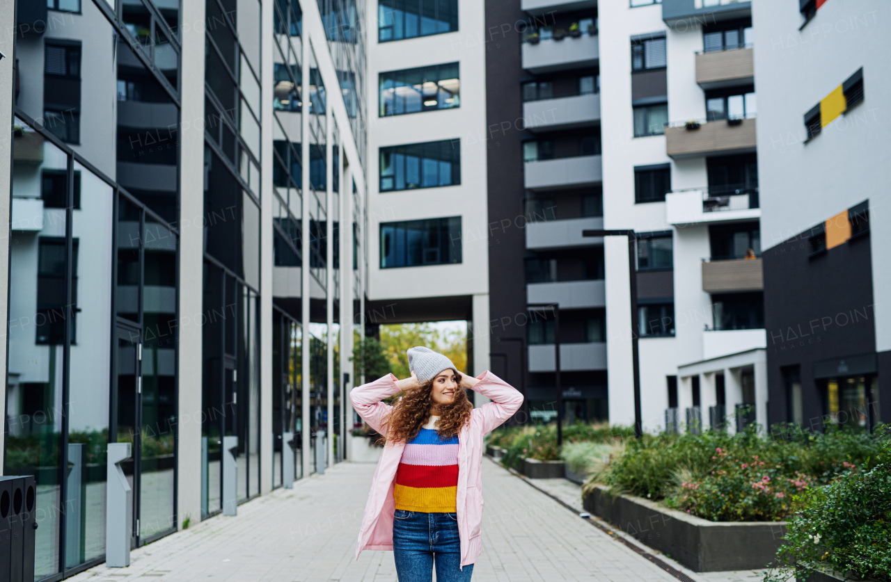 Front view portrait of young woman standing outdoors by block of flats in city.