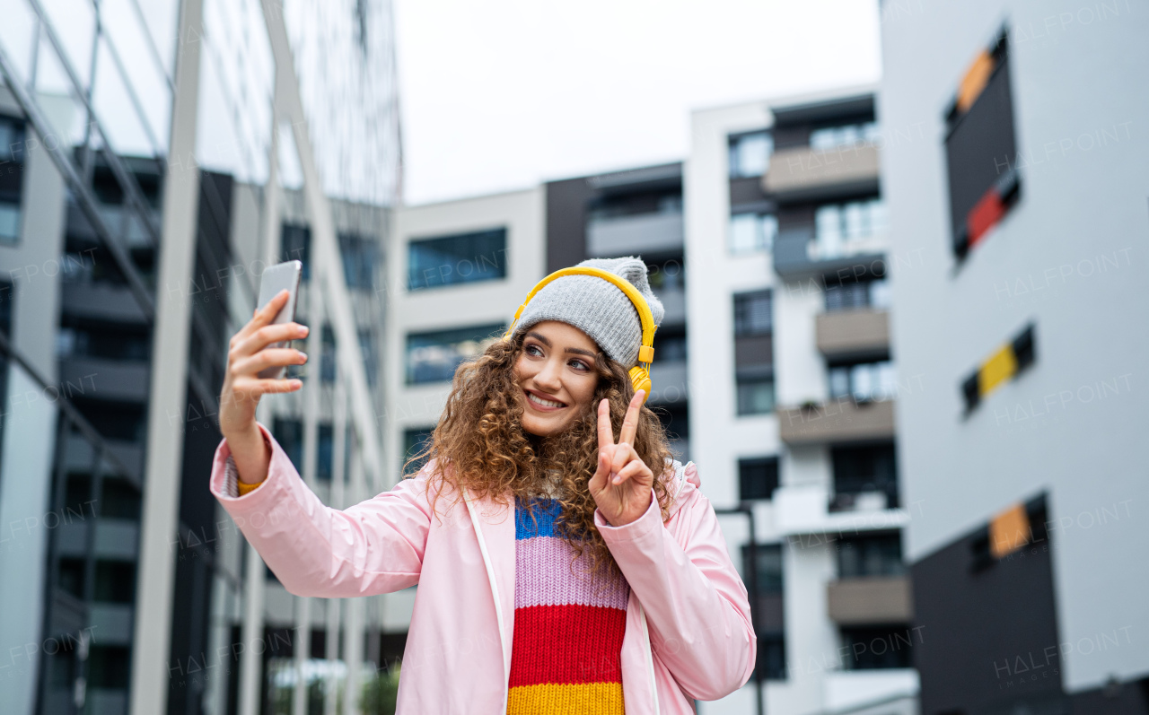 Portrait of young woman with smartphone making video for social media outdoors on street.