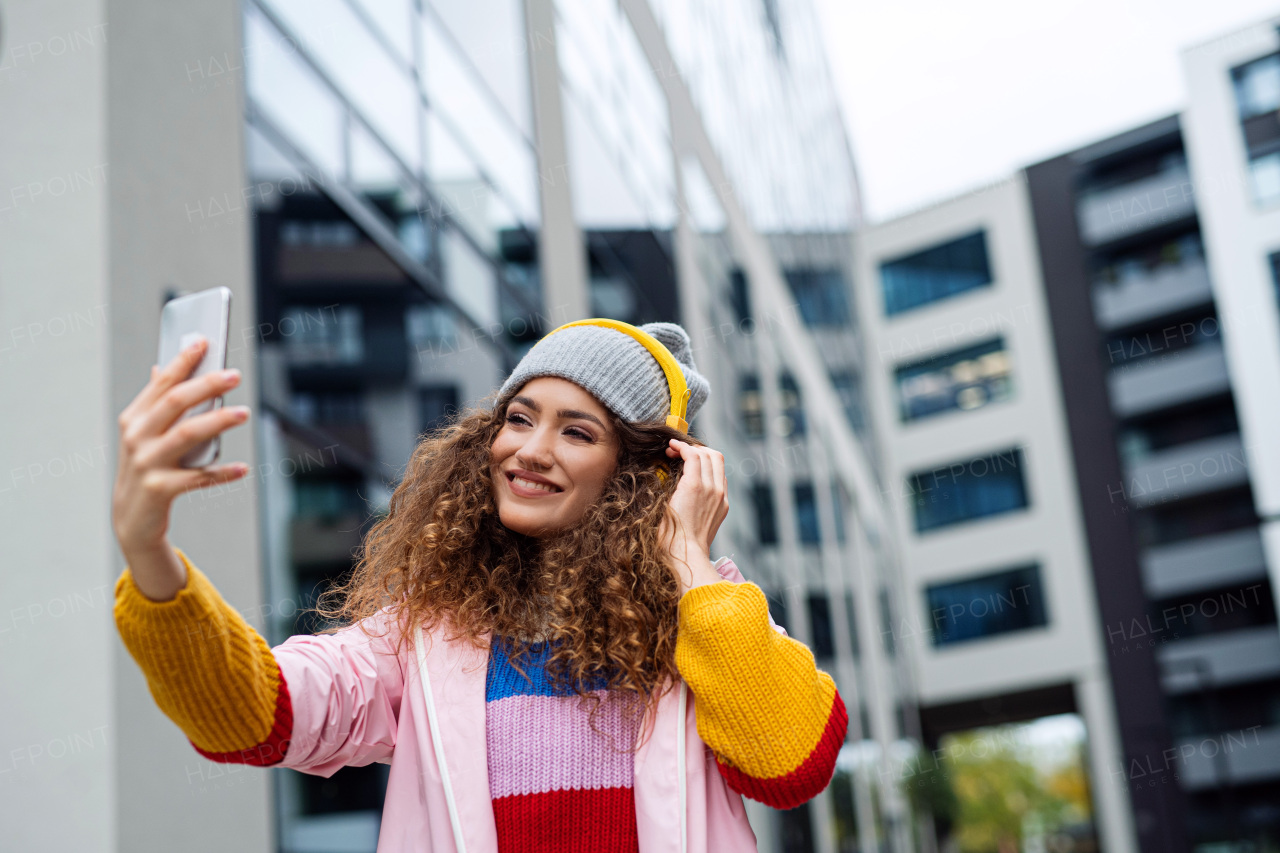 Portrait of young woman with smartphone making video for social media outdoors on street.