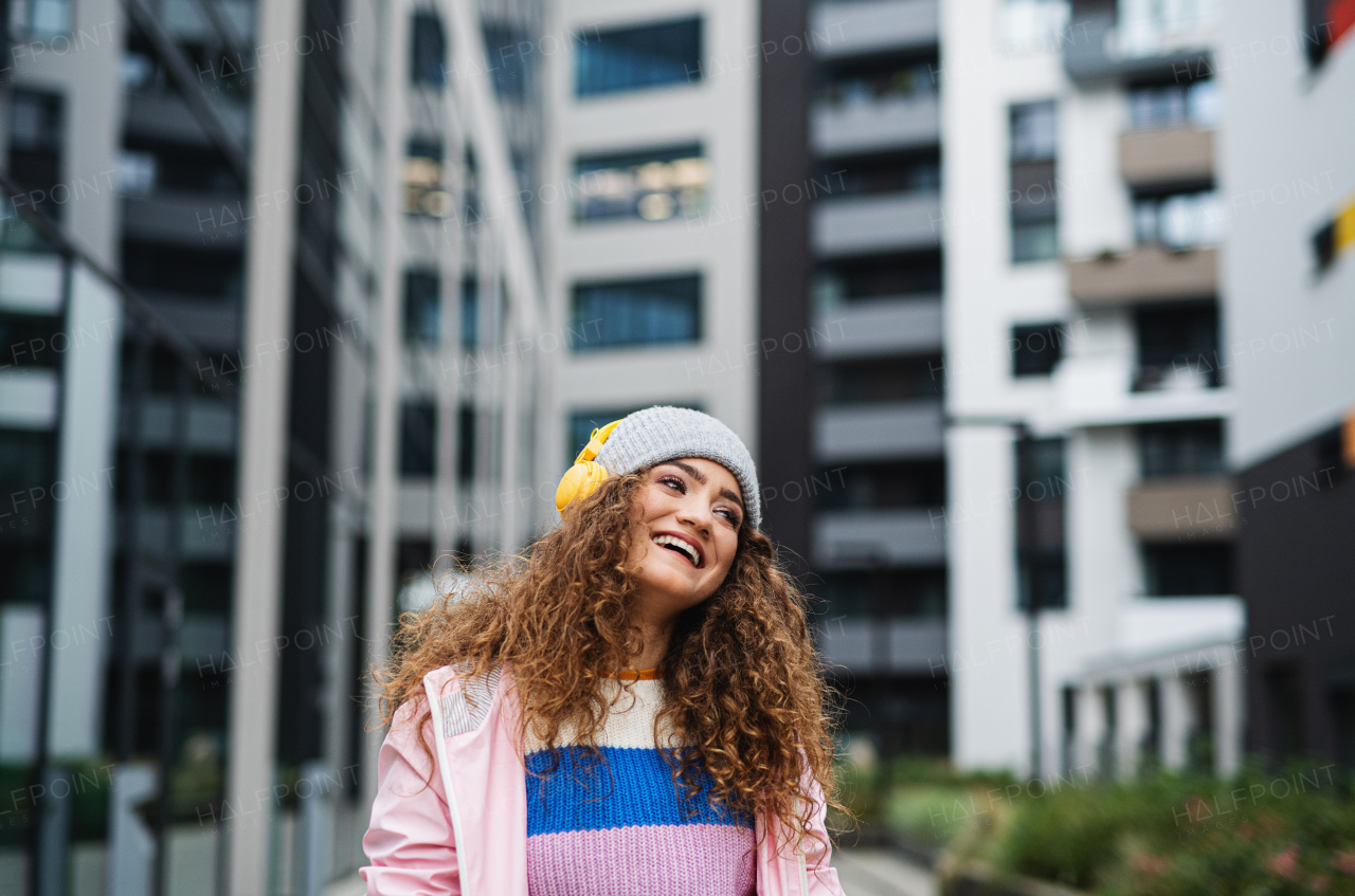 Happy young woman with headphones outdoors on street, listening to music.