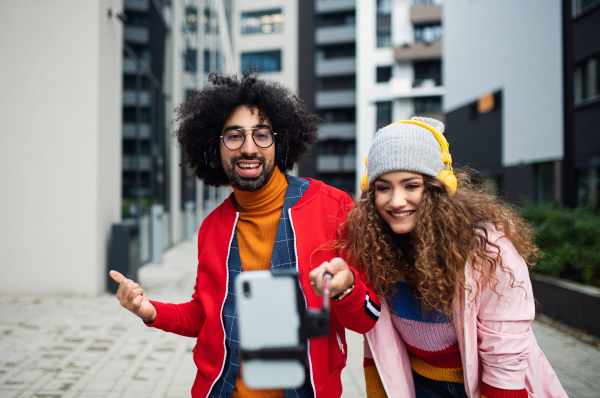 Portrait of young couple with smartphone making video for social media outdoors on street.