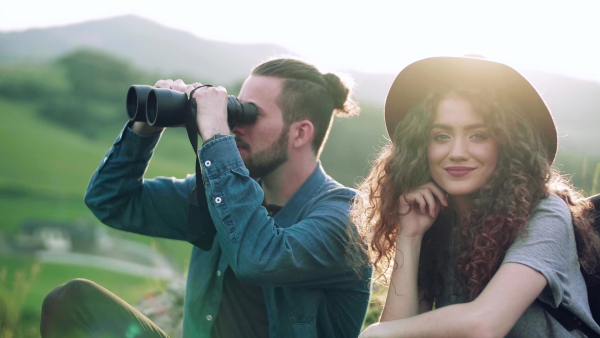 Young tourist couple travellers with binoculars hiking in nature, sitting and resting.