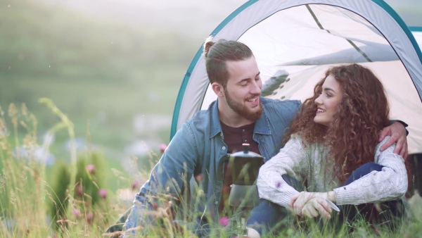 A young tourist couple travellers with tent shelter sitting in nature, resting.