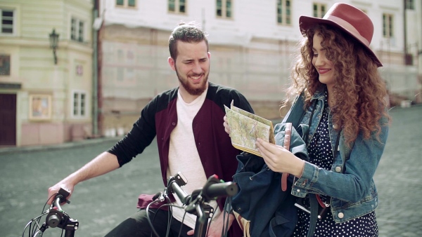 Young tourist couple travellers with map and scooters in small town, sightseeing. Slow motion.