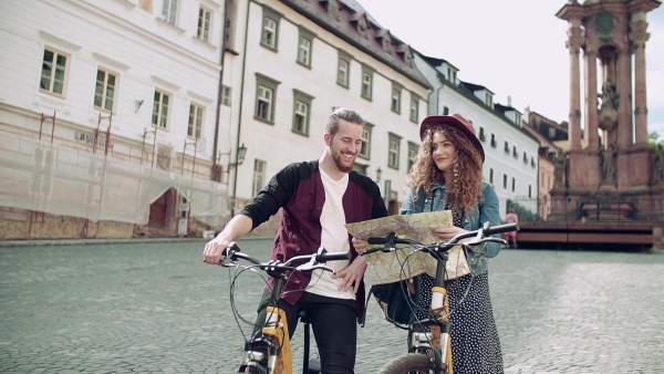 Young tourist couple travellers with map and scooters in small town, sightseeing. Slow motion.