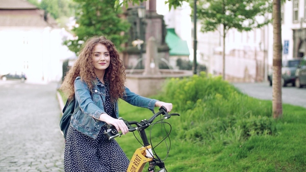 Beautiful young woman tourist traveller with electric scooter in small town, sightseeing. Slow motion.