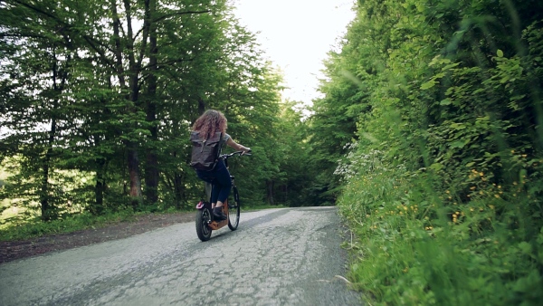 Rear view of young tourist couple travellers with backpacks and electric scooters in nature. Slow motion.