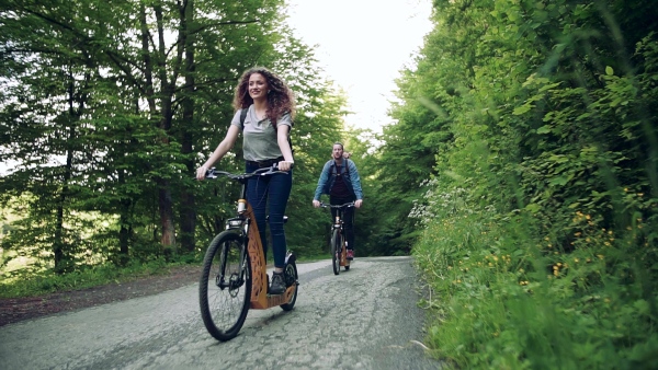 Young tourist couple travellers with backpacks riding electric scooters in nature. Slow motion.