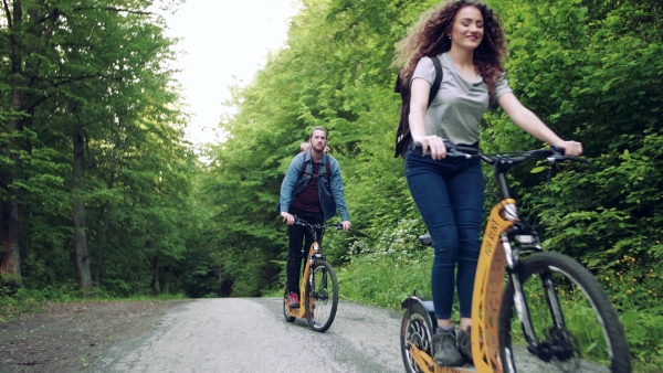 Young tourist couple travellers with backpacks riding electric scooters in nature.