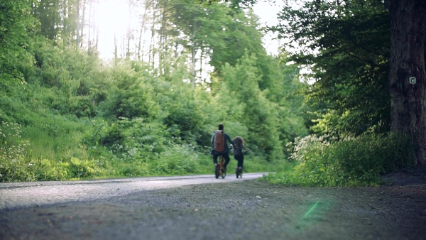 Rear view of young tourist couple travellers with backpacks and electric scooters in nature. Slow motion.