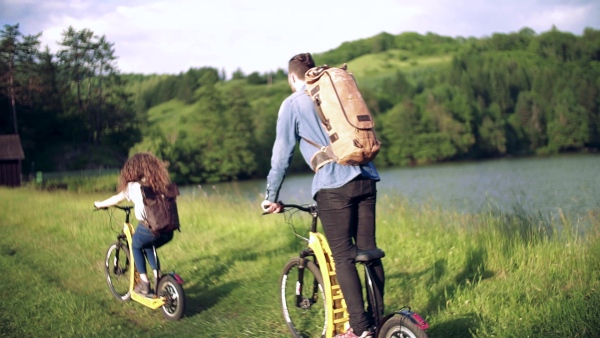 Rear view of young tourist couple travellers with backpacks and electric scooters in nature. Slow motion.