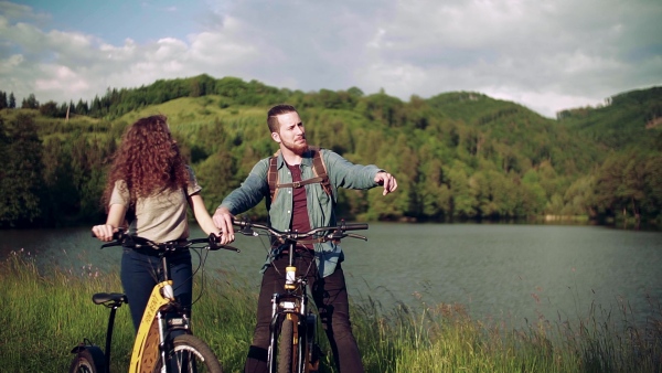 Young tourist couple travellers with electric scooters in nature, standing by lake. Slow motion.