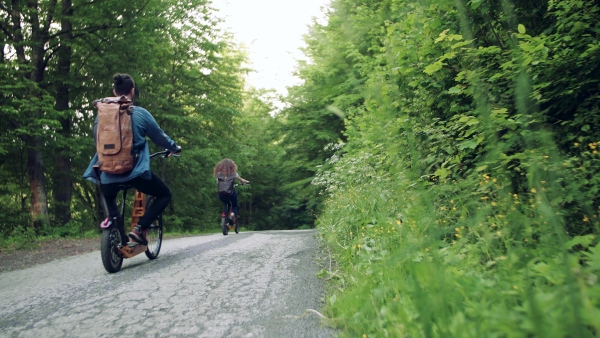 Rear view of young tourist couple travellers with backpacks and electric scooters in nature.