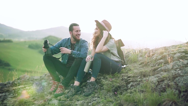 Young tourist couple travellers with binoculars hiking in nature, sitting and resting. Slow motion.