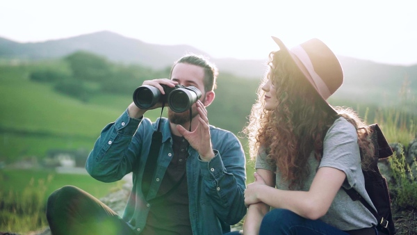 Young tourist couple travellers with binoculars hiking in nature, sitting and resting. Slow motion.