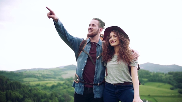 A young tourist couple travellers with backpacks hiking in nature, talking. Slow motion.