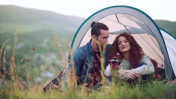 A young tourist couple travellers with tent shelter sitting in nature, resting. Slow motion.