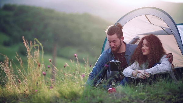 A young tourist couple travellers with tent shelter sitting in nature, resting. Slow motion.