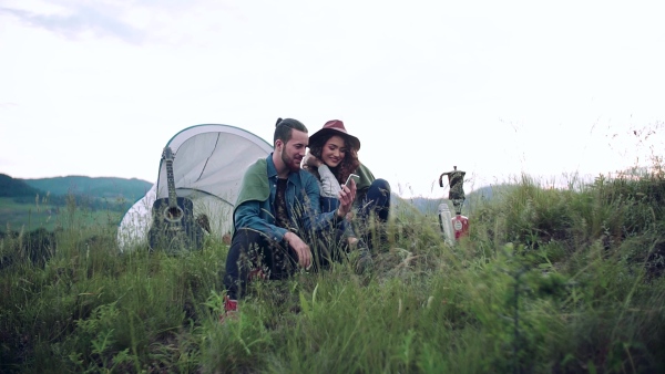 A young tourist couple travellers with tent shelter and smartphone sitting in nature, resting. Slow motion.