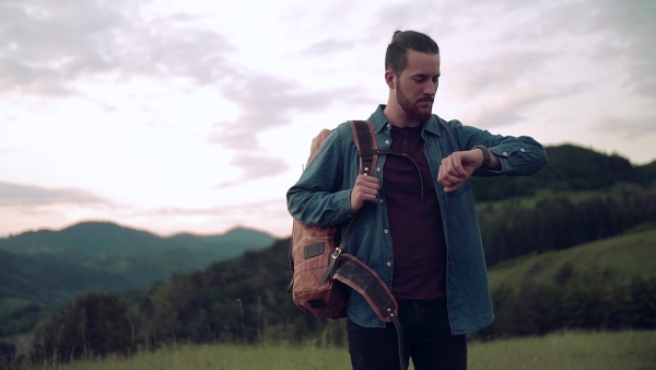 Young man tourist traveller with backpack hiking in nature, checking the time. Slow motion.