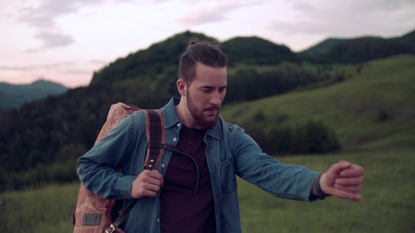 Young man tourist traveller with backpack hiking in nature, checking the time. Slow motion.